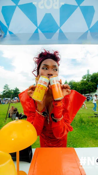 Een persoon in een rode outfit toont twee BOS Ice Tea-blikjes